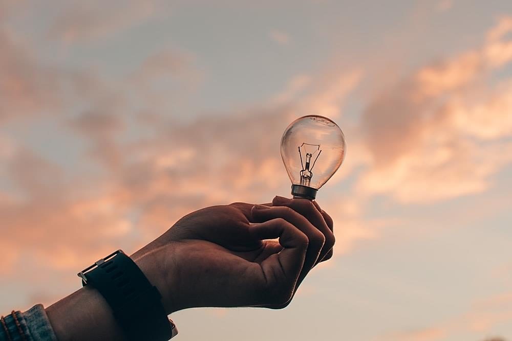 Hand holding a lightbulb against a sunset sky